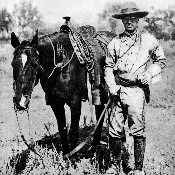 Theodore Roosevelt in fringed buckskin jacket posing with a horse in the Dakota Badlands, circa 1885